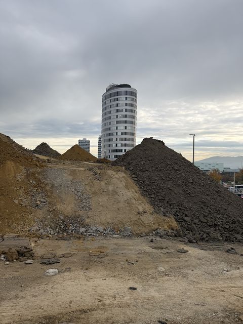 Hohe Halden aus Erde und Gestein, dahinter ein rundes Hochhaus