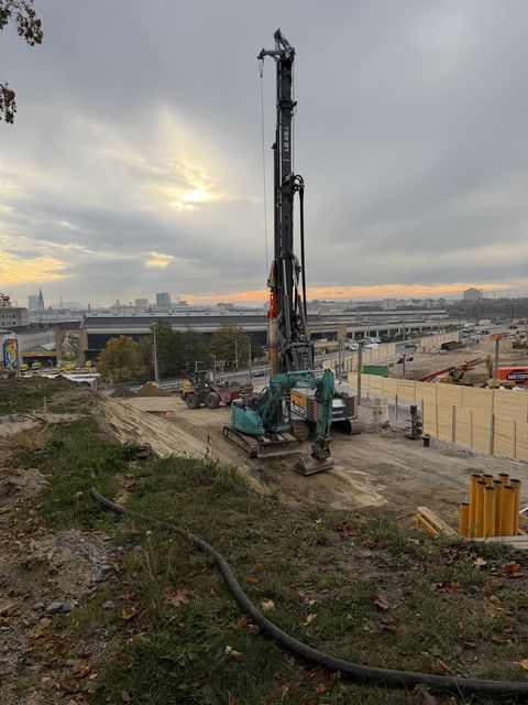Ein hohes Bohrgerät auf der Baustelle, dahinter der Bahnhofsbereich unter bewölktem Himmel